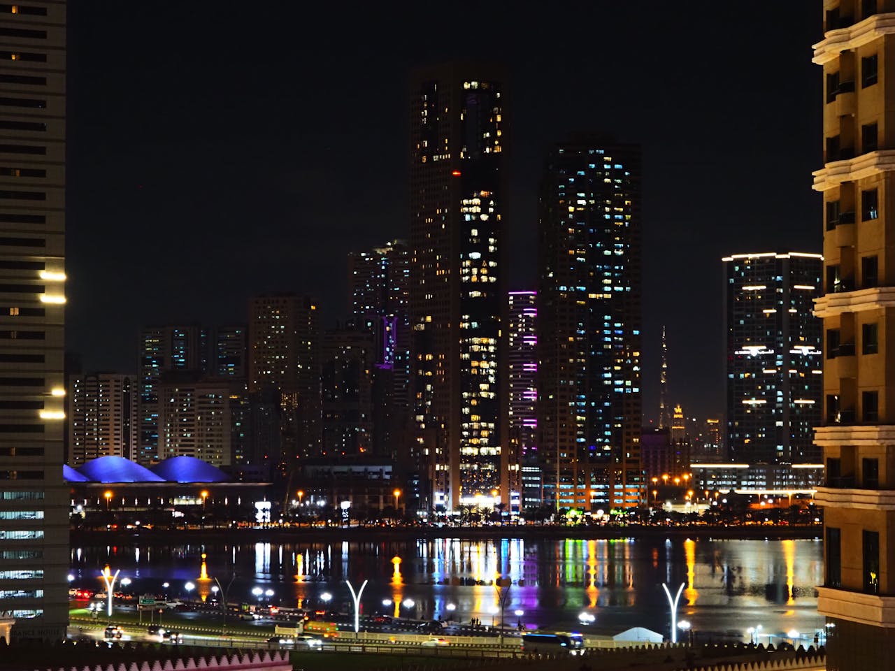 Stunning night view of a vibrant city skyline with illuminated skyscrapers and water reflections.